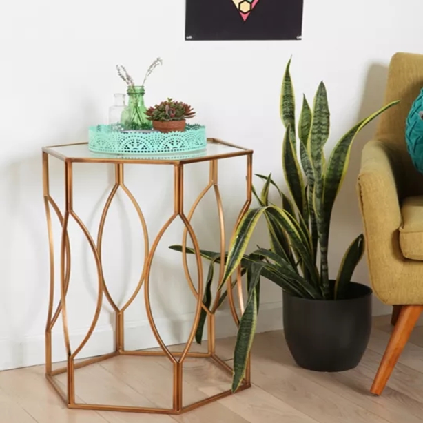 Anat Luxury Hexagonal Glass Side Table Anat Luxury hexagonal side table with a clear glass top and a stylish, intertwined oval-patterned gold metal base. Accent furniture available near Ambala, Haryana, and across India.