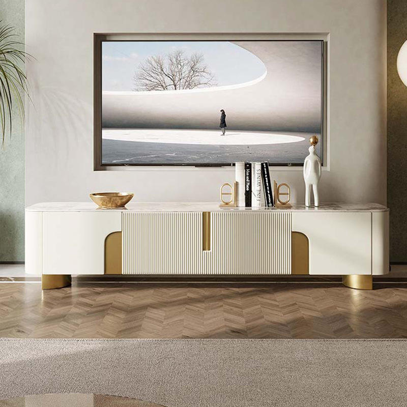 Anat Urbane Gloss TV Stand Anat Urbane luxury TV console unit featuring a long, low profile with a white/cream marble-look top, a central ribbed door/drawer panel, side cut-outs with gold backing, and low gold metal feet. Luxury furniture available near Ambala, Haryana, and across India.