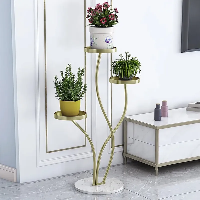 Anat Verona Triple-Tier Plant Stand Anat Verona modern three-tiered indoor plant stand featuring three gracefully curving gold metal stems supporting round gold tray shelves, anchored by a round white marble base. Decorative furniture available near Ambala, Haryana, and across India.
