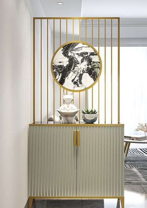 Anat Aria with Modern Gold Steel Partition Anat Aria luxury storage cabinet with reeded/fluted light grey doors and gold handles, topped by a built-in vertical gold stainless steel partition and a circular black and white marble wall accent. Luxury furniture available near Ambala, Haryana, and across India.