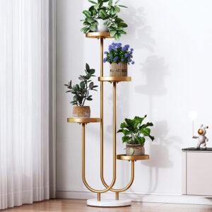 Anat Luxor modern four-tiered indoor plant stand featuring a tall gold metal frame with curved base supports and four round gold tray shelves at staggered heights, standing on a white marble base. Decorative furniture available near Ambala, Haryana, and across India.