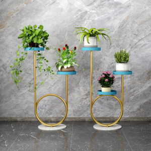 Anat Rosé Gold set of two curved, triple-tiered indoor plant stands featuring a looped gold metal frame, round blue shelves, and a white marble base. Decorative furniture available near Ambala, Haryana, and across India.