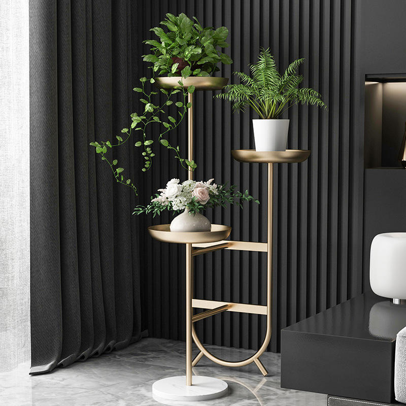 Anat Solis Triple Tier Plant Stand Anat Solis modern triple-tier plant stand featuring a tall gold metal frame with three round tray-style shelves at varying heights, supported by a round white marble base. Decorative furniture available near Ambala, Haryana, and across India.
