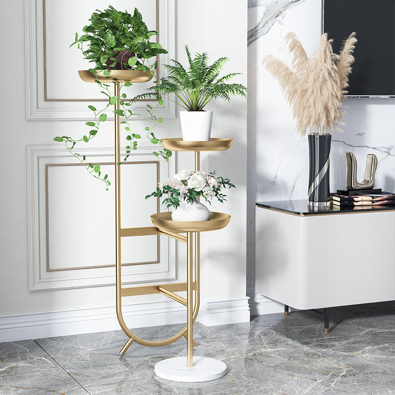 Anat Solis Triple Tier Plant Stand Anat Solis modern triple-tier plant stand featuring a tall gold metal frame with three round tray-style shelves at varying heights, supported by a round white marble base. Decorative furniture available near Ambala, Haryana, and across India.