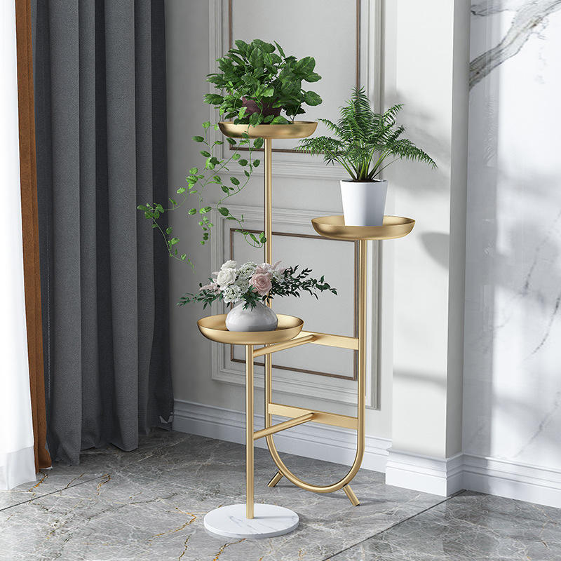 Anat Solis Triple Tier Plant Stand Anat Solis modern triple-tier plant stand featuring a tall gold metal frame with three round tray-style shelves at varying heights, supported by a round white marble base. Decorative furniture available near Ambala, Haryana, and across India.