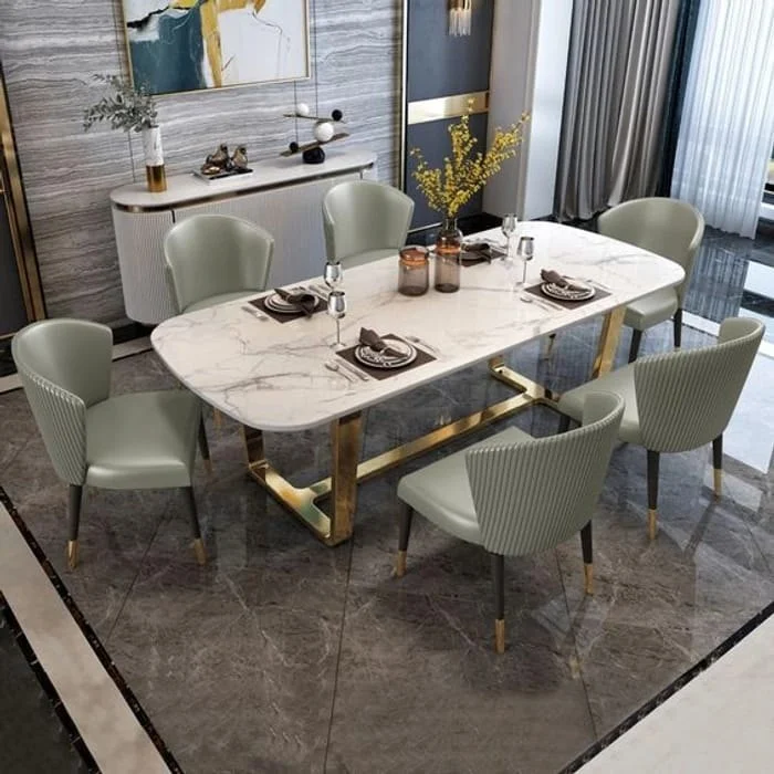 Anat Opulent Luxe Dining Ensemble Anat Opulent Luxe modern dining set featuring a rectangular white marble-look top, a polished gold metal base, and six sage green/gray upholstered dining chairs. Luxury dining furniture available near Ambala, Haryana, and across India.